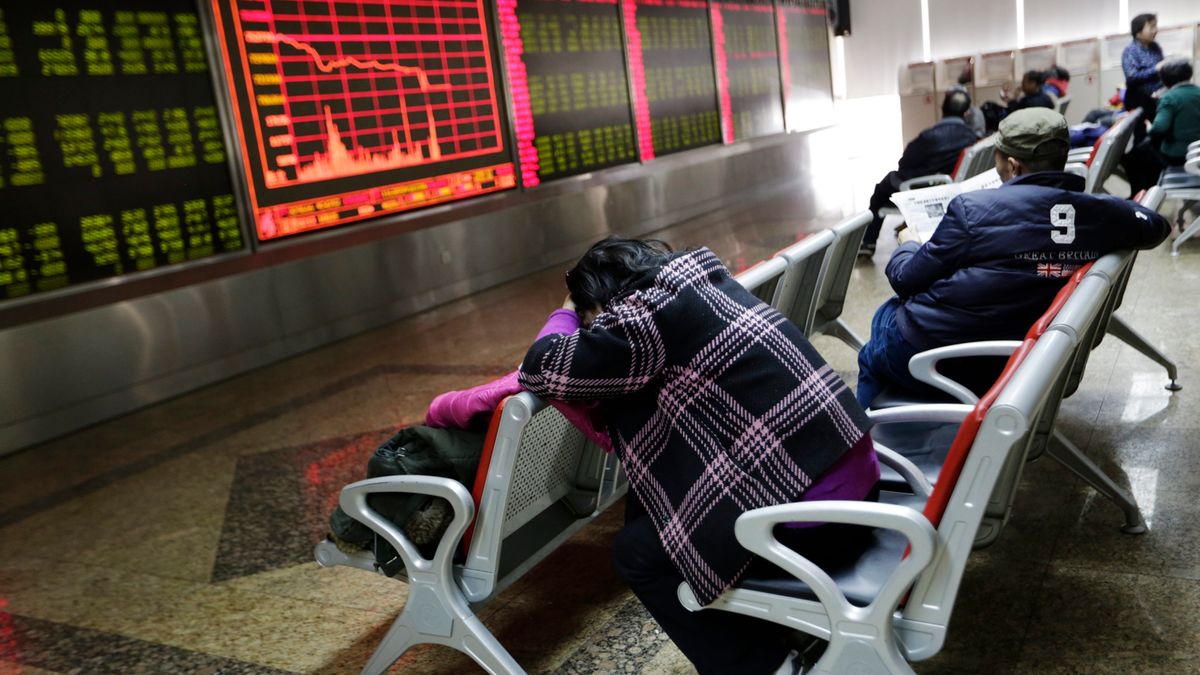 Chińscy inwestorzy śledzą ekran pokazujący spadek na giełdzie.