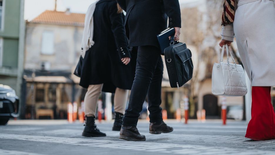 A group of businesspeople captured mid-stride, engaged in a conversation while heading to an outdoor meeting on a sunny winter day.