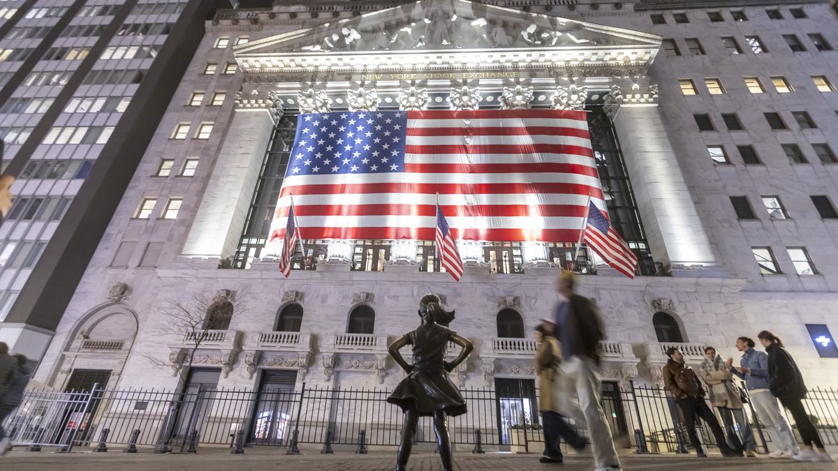 The Fearless Girl bronze sculpture by Kristen Visbal, stands across the New York Stock Exchange building and people are passing by. Night view of the illuminated exterior of New York Stock Exchange with a big American flag from the front facade. NYSE building has the style of classical architecture of Greece with columns, the inscription New York Stock Exchange and US flags hanging. The financial organization at Wall Street is a symbol for the global and American Economy as one of the most powerful financial institution located in Wall Street at lower Manhattan in New York City, United States of America. The US stock market is reacting with heavy losses after president Trump tariffs announcement on April 2025. November 2024 in NYC, USA  (Photo by Nicolas Economou/NurPhoto via Getty Images)