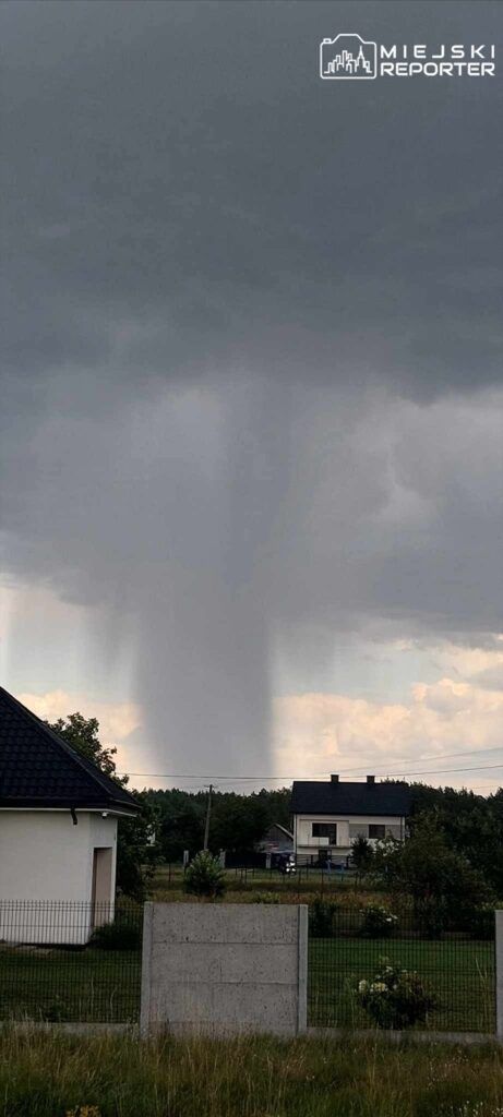 Intensywne opady deszczu spływające z chmur nad domami w podmiejskim krajobrazie.