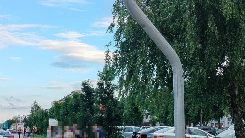 Znak drogowy informujący o ścieżce dla pieszych i rowerzystów, w tle grupa ludzi na chodniku obok zaparkowanych samochodów.