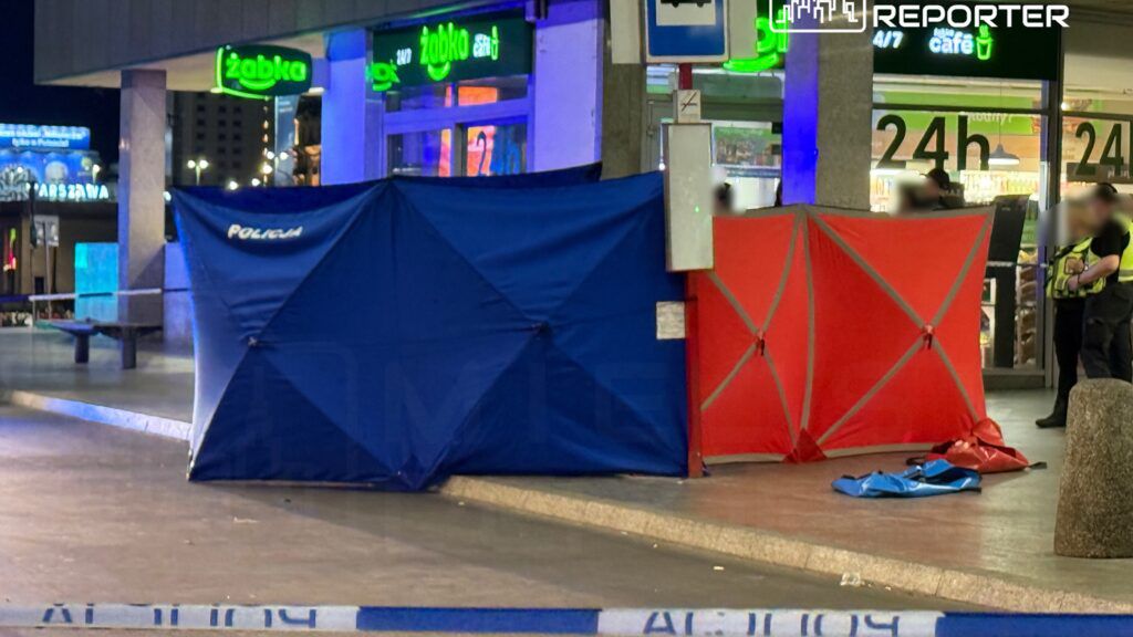 Policjanci zabezpieczają miejsce zdarzenia, gdzie rozłożone są niebieskie i czerwone namioty, obok sklepu Żabka.