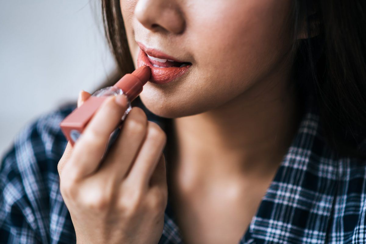 Close up portrait of woman touching her lips with lipstick.