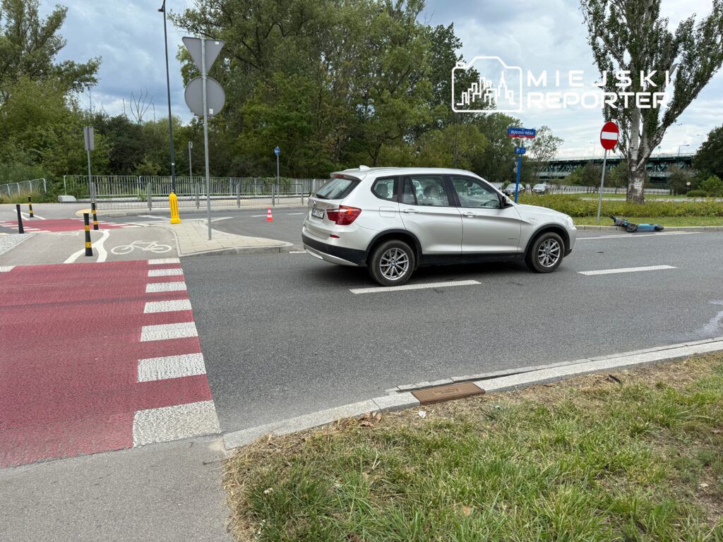 Samochód osobowy przejeżdża przez skrzyżowanie z rowerowym pasem w otoczeniu zieleni i znaków drogowych.