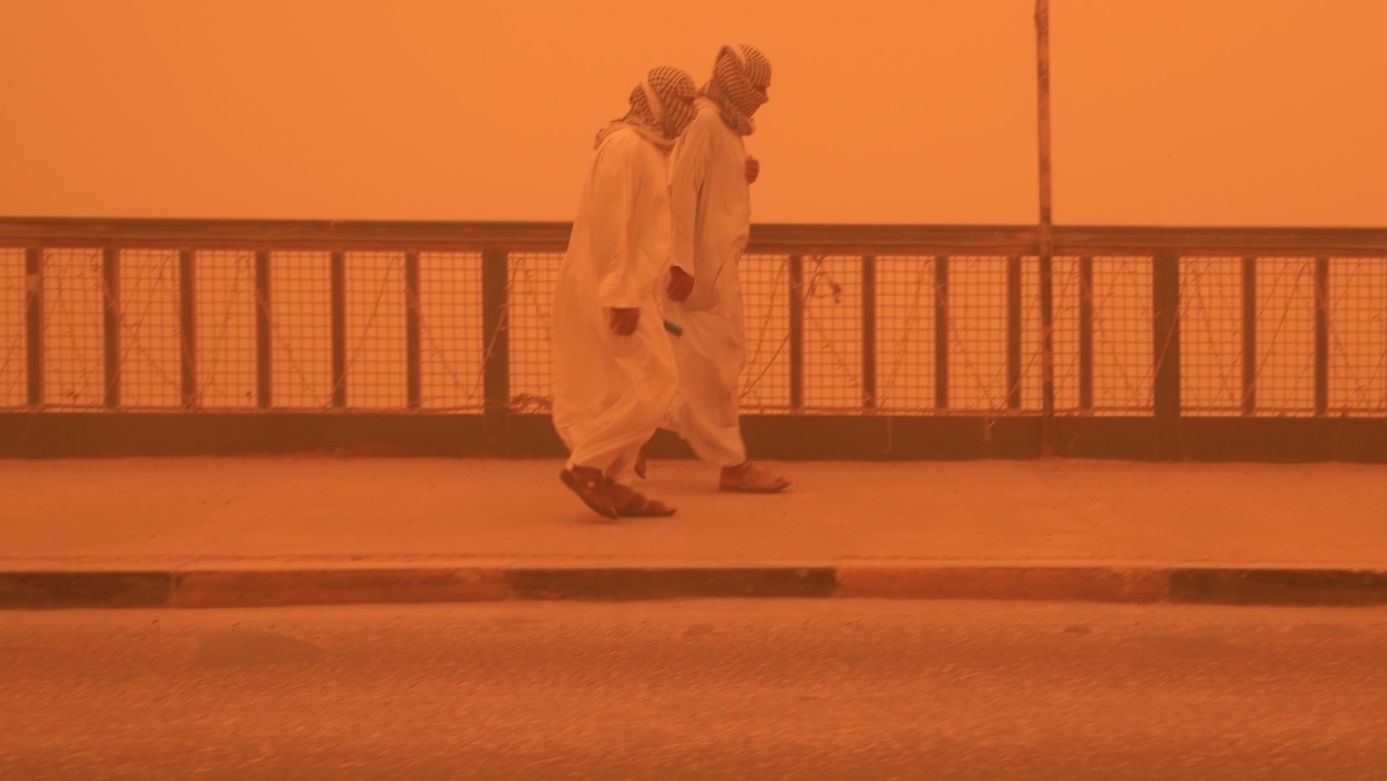 Ludzie chroniący twarze podczas burzy piaskowej w Bagdadzie 16 maja 2022 r. 