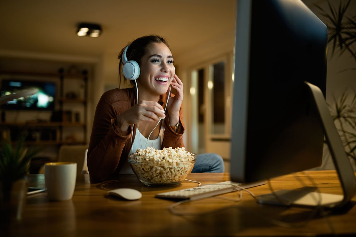 Happy,Woman,Eating,Popcorn,And,Watching,Movie,On,Desktop,Pc
woman,movie,popcorn,headphones,snack,using computer,young adult,