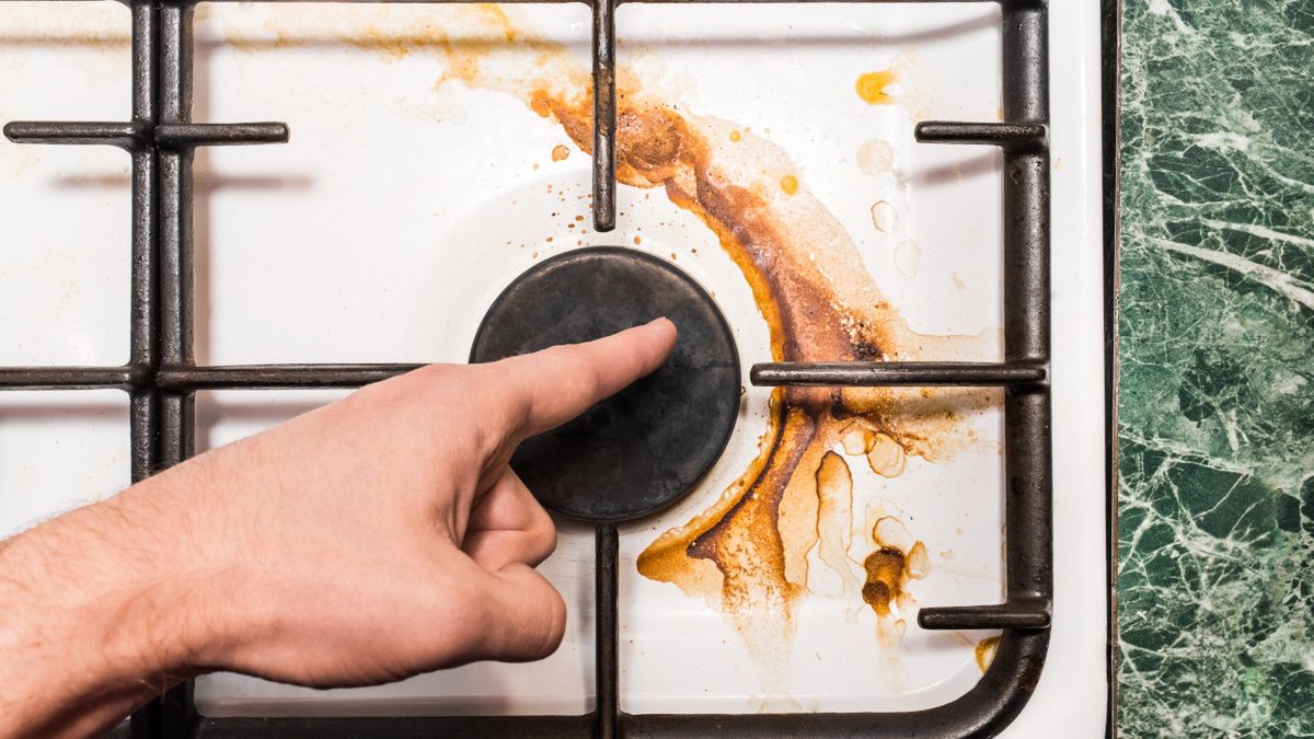 Dłoń wskazująca na brudny palnik kuchenki gazowej