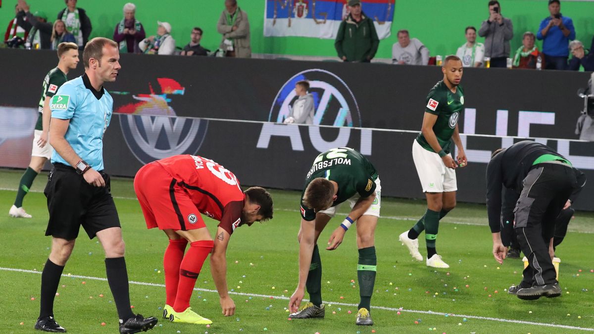 piłkarze VfL Wolfsburg i Eintrachtu Frankfurt zbierają gumowe piłki wrzucone na boisko przez kibiców