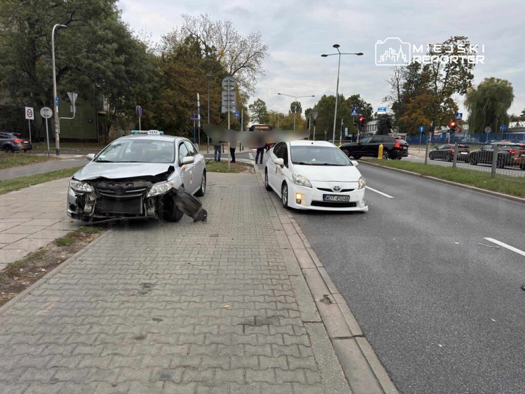 Dwa uszkodzone samochody osobowe zaparkowane na chodniku, jeden z nich to taksówka z uszkodzoną przednią częścią.