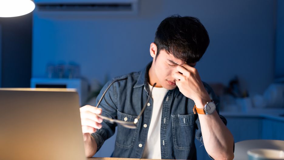 Tired overworked asian male feeling eyes strain after using computer while working at home