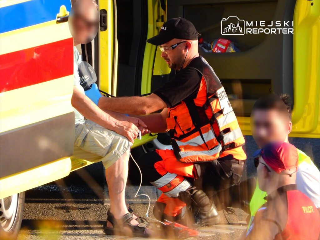 Ratownik medyczny udziela pomocy mężczyźnie siedzącemu w pobliżu karetki na drodze.