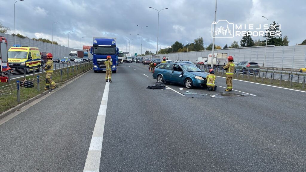 Strażacy udzielają pomocy przy wypadku drogowym na autostradzie, obok uszkodzonego samochodu osobowego.