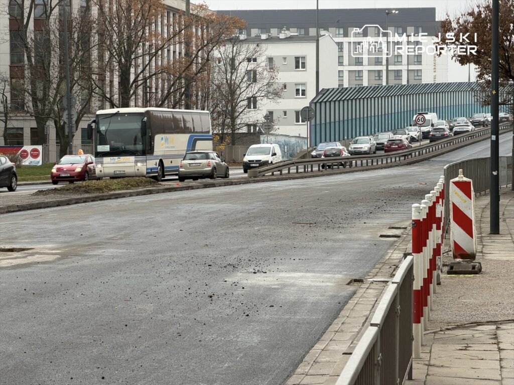 Autobus wypełniony pasażerami zatrzymany na pasie drogowym, obok ruchliwej jezdni z samochodami osobowymi.