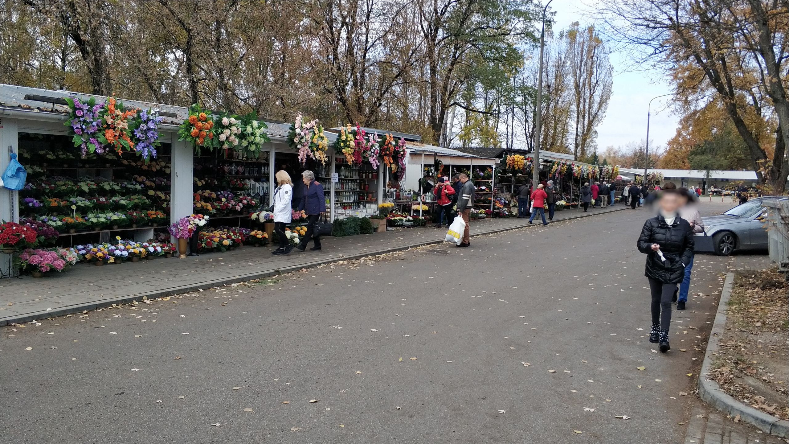 Zdjęcie przedstawia stoiska z kwiatami i odwiedzających cmentarz