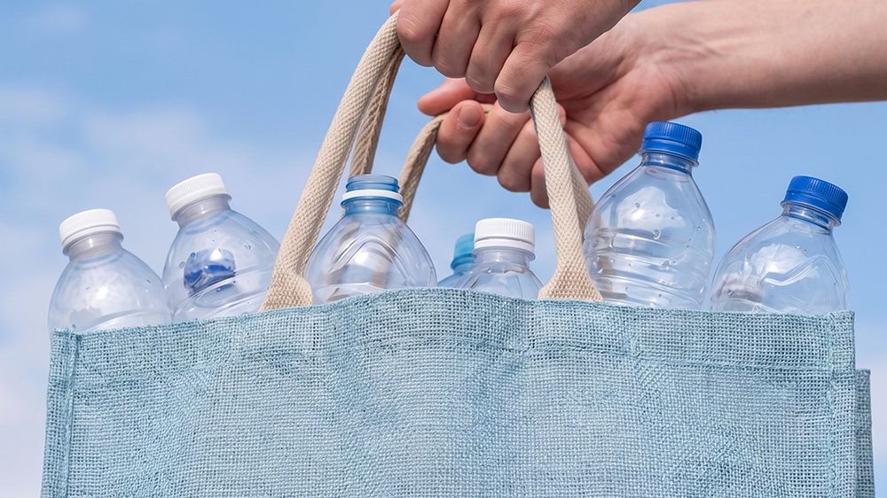 Osoba trzymająca torbę z pustymi butelkami plastikowymi do zwrotu. - tytułowa