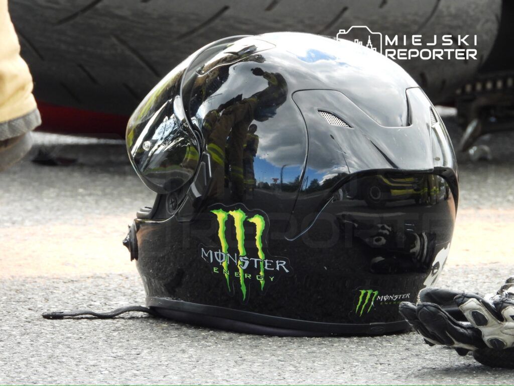 Czarny kask motocyklowy z logo Monster Energy leży na asfalcie obok rękawicy ochronnej.
