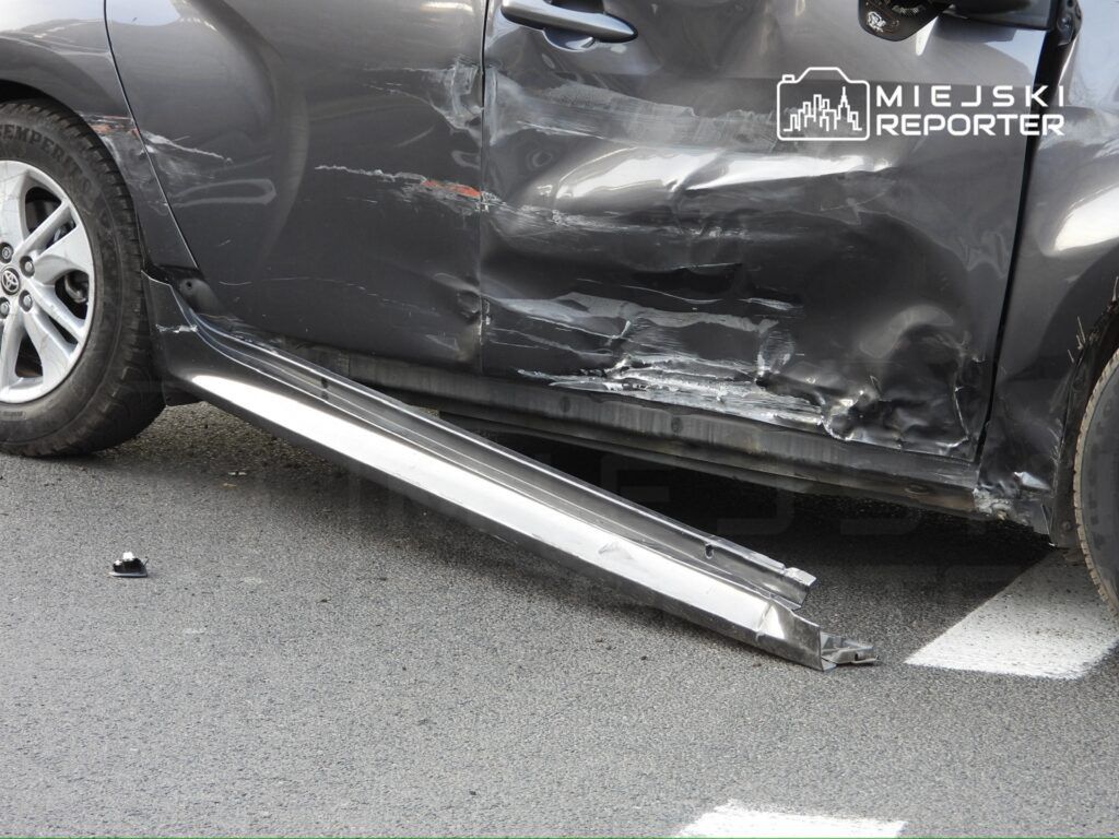 Uszkodzony samochód osobowy z wgniecioną boczną częścią i zdemontowanym progiem na asfaltowej nawierzchni.