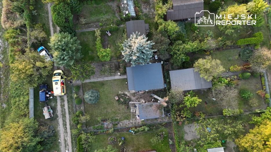 Karetka i radiowóz na drodze w otoczeniu działek i zieleni, w tle widać domki letniskowe.