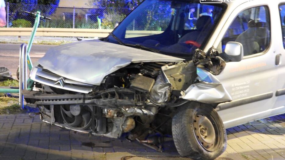 Uszkodzony samochód osobowy zaparkowany na chodniku, z widocznymi wgnieceniami z przodu i uszkodzoną karoserią.