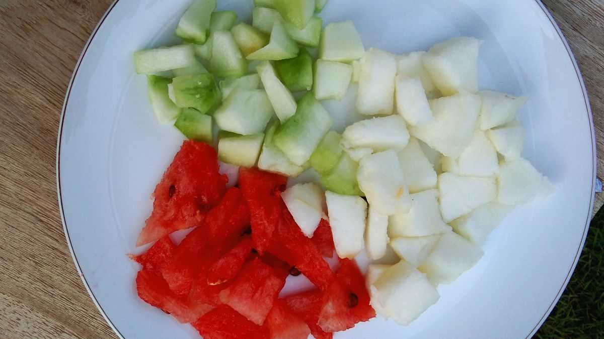 Fresh watermelon (Citrullus lanatus), melon (Cucumis melo) and cucumber pieces (Cucurbitaceae) on a white plate against a background of antique wood or rustic woodAr razzaq