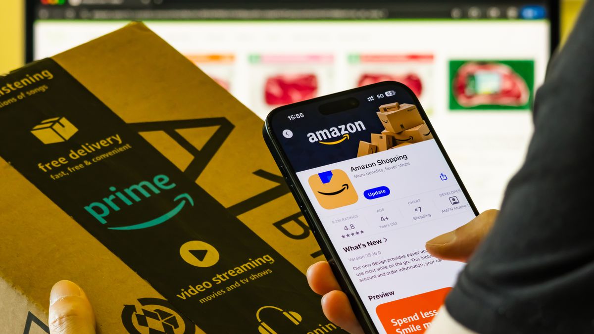 CHONGQING, CHINA - AUGUST 22: In this photo illustration, a person holds a smartphone displaying the Amazon Shopping app page in the Apple App Store in one hand and an Amazon Prime-branded delivery box in the other hand, with a computer screen showing the Amazon website in the background on August 22, 2025 in Chongqing, China. (Photo illustration by Cheng Xin/Getty Images)