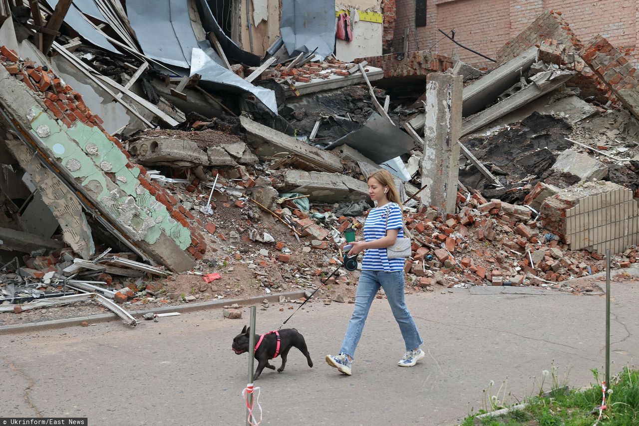 Kobieta spaceruje z psem obok budynku zniszczonego przez rosyjski ostrzał, Okhtyrka, region Sumy, północno-wschodnia Ukraina