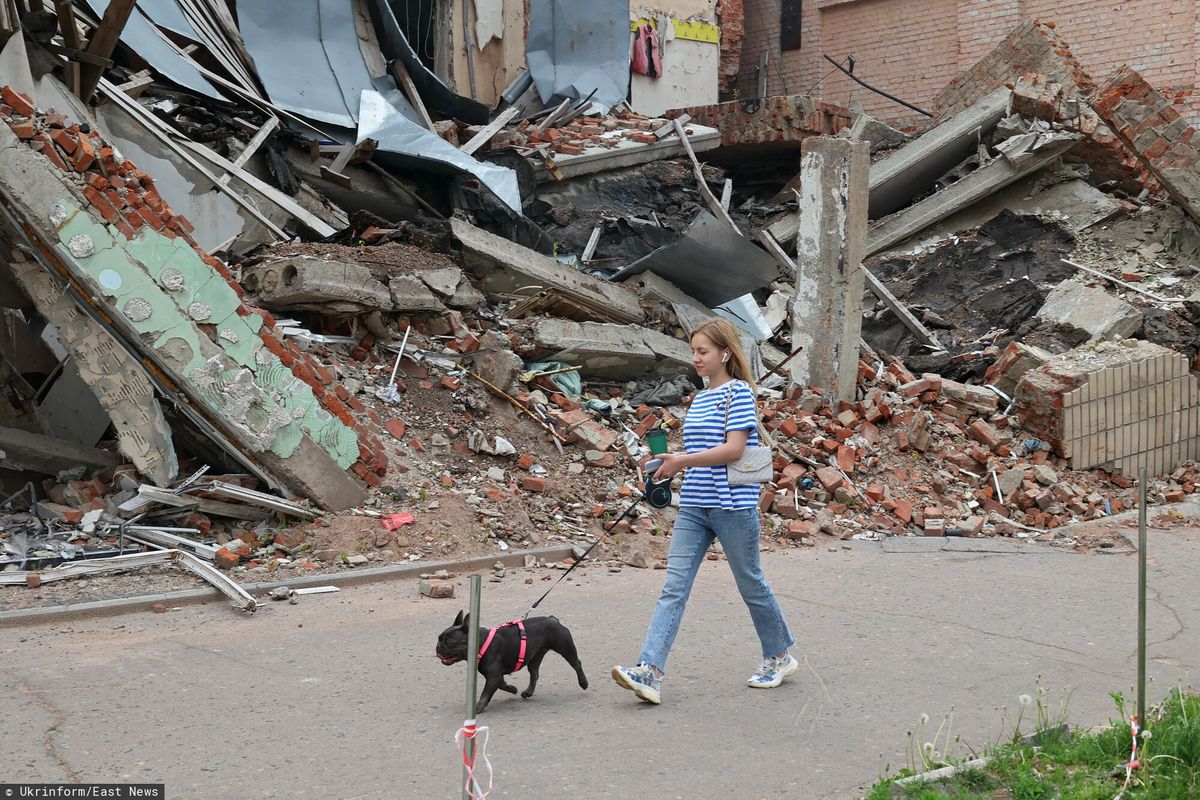 Kobieta spaceruje z psem obok budynku zniszczonego przez rosyjski ostrzał, Okhtyrka, region Sumy, północno-wschodnia Ukraina