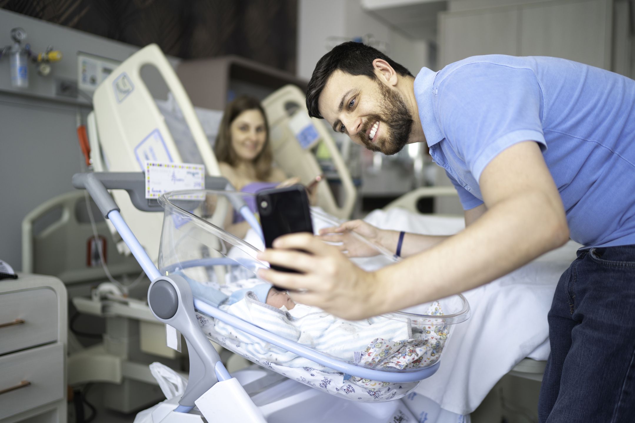 Happy father taking a selfie of his newborn and wife in the hospital