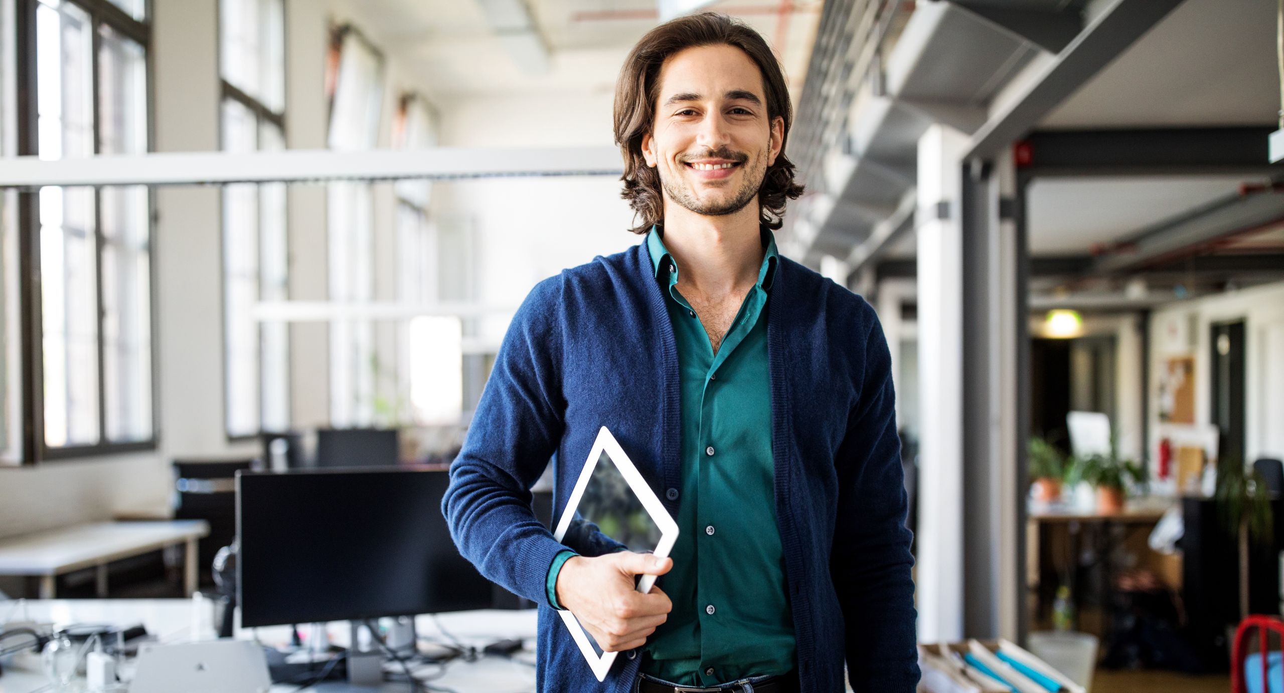 Smiling businessman standing with digital tabletPortrait of smiling young handsome businessman standing with digital tablet at creative officeLuis Alvarez