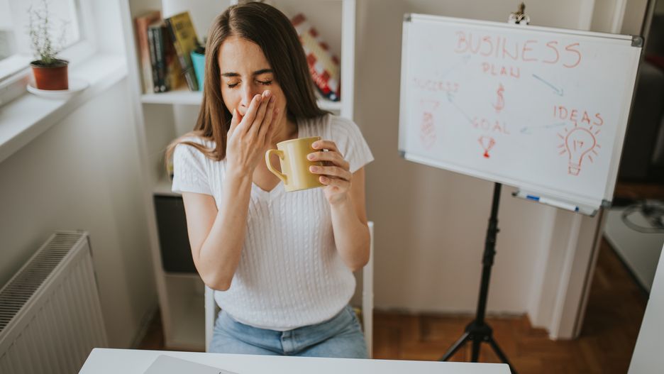 Tired woman is yawning while holding coffee.