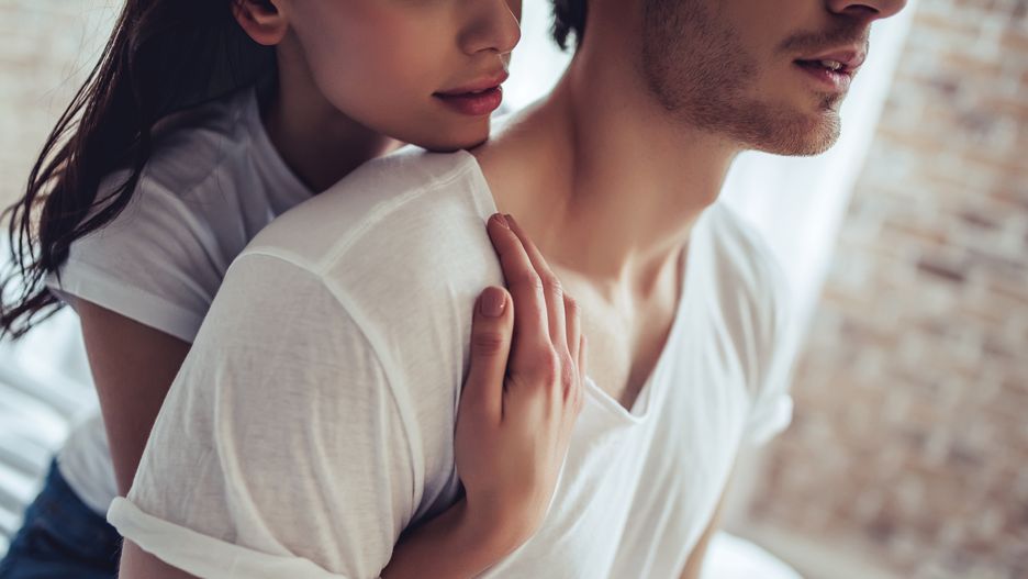 Cropped image of beautiful young couple is sitting on bed in bedroom. Enjoying spending time together at home.
