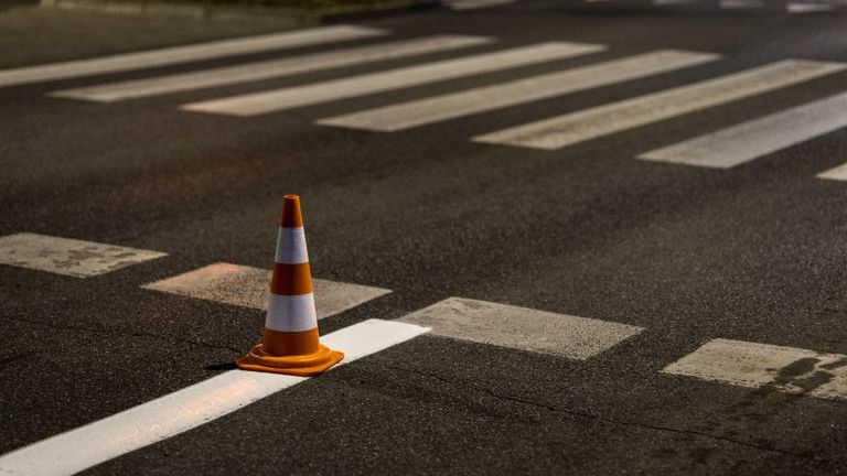 Pomarańczowy stożek drogowy umieszczony na przejściu dla pieszych na ciemnej nawierzchni ulicy.