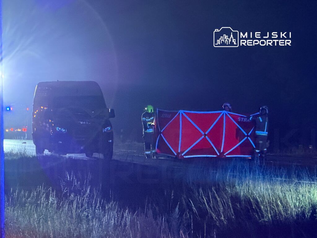 Ratownicy w kamizelkach odblaskowych przygotowują się do zabezpieczenia miejsca wypadku na drodze nocą.