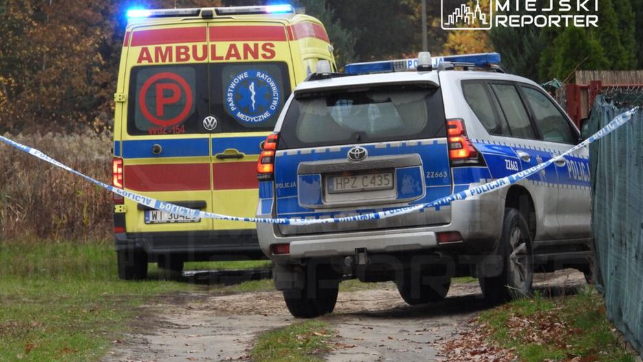 Karetka pogotowia i radiowóz policji stoją na leśnej drodze, oznaczone taśmą zabezpieczającą.