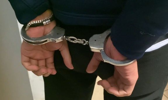 Mężczyzna z rękami skuty w kajdanki stoi w zamkniętym pomieszczeniu.