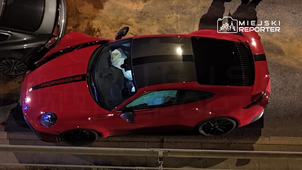 Czerwone Porsche zaparkowane w nocy na ulicy, obok szarego samochodu.