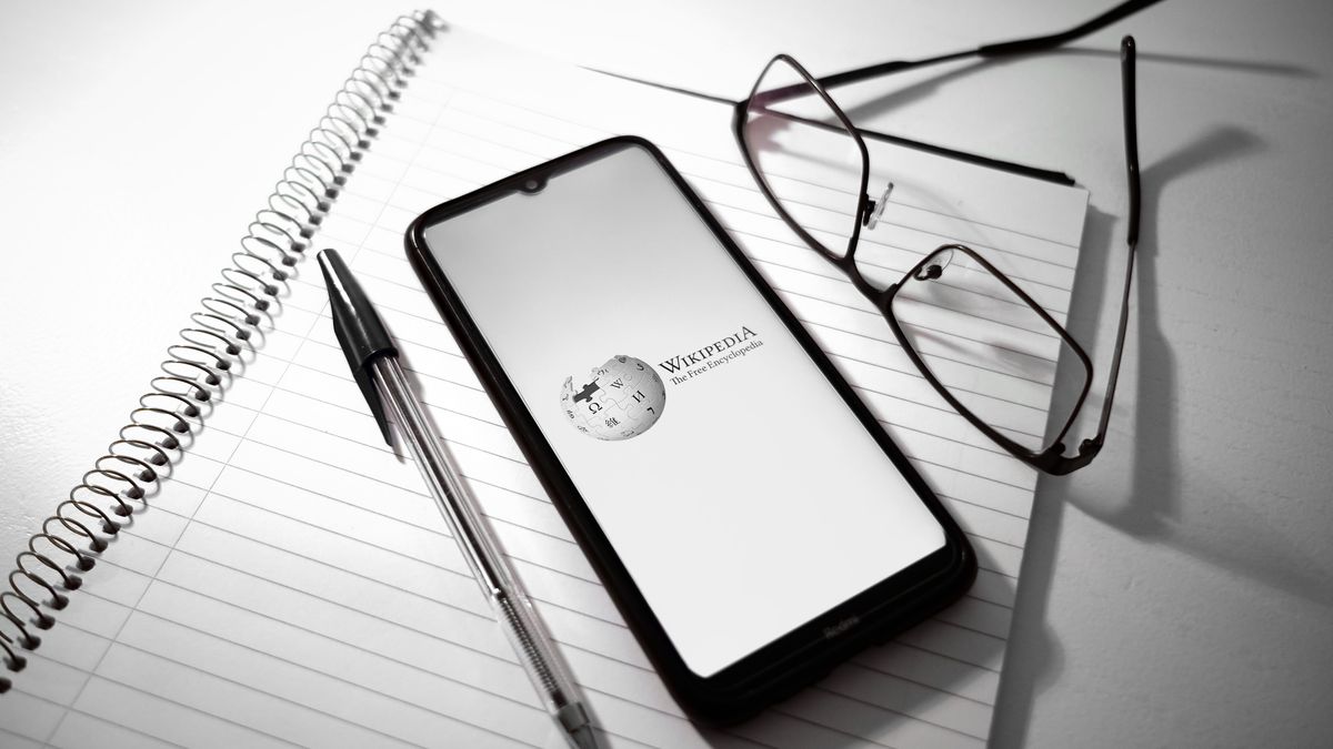 In this photo illustration a Wikipedia logo is displayed on a smartphone screen above a notebook next to a pen and glasses in Athens, Greece on February 27, 2023. (Photo illustration by Nikolas Kokovlis/NurPhoto via Getty Images)