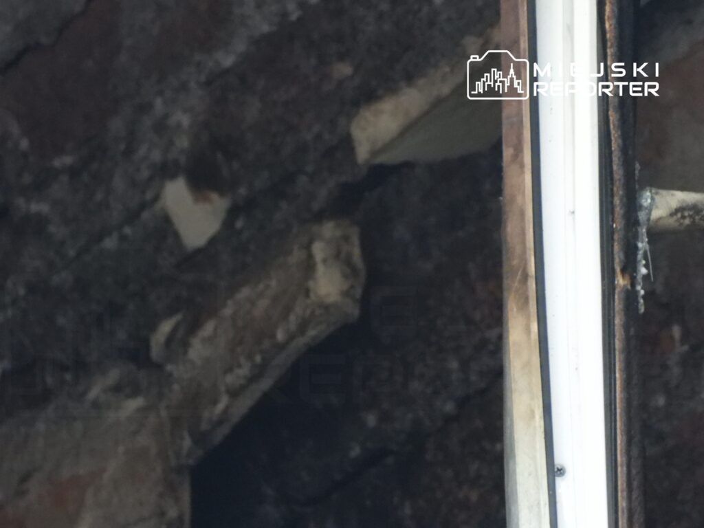 Uszkodzony sufit z widocznymi fragmentami tynku i drewnianymi belkami w zaciemnionym pomieszczeniu.