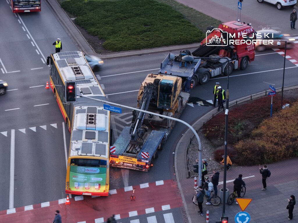 Kierowca autobusu stoi obok zatrzymanego pojazdu na skrzyżowaniu, podczas gdy policjanci kierują ruchem.