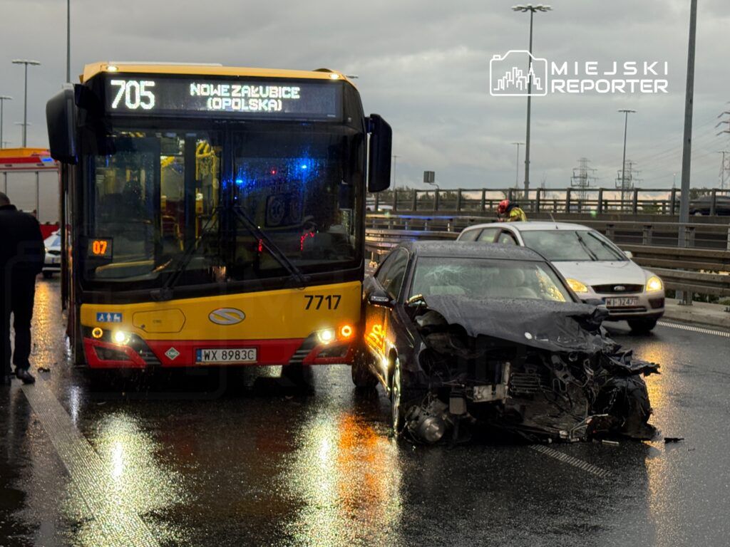 Autobus komunikacji miejskiej zatrzymany obok uszkodzonego samochodu osobowego na mokrej jezdni.