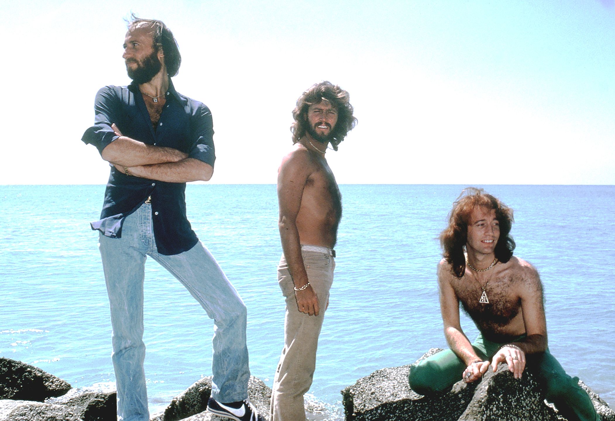 The Bee Gees (Barry, Maurice and Robin Gibb) pose on rocks overlooking the ocean in Florida in 1979. (Photo by Bonnie Schiffman/Getty Images)