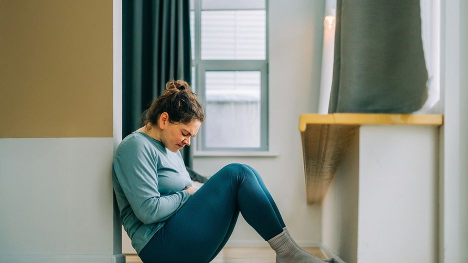 Young woman suffering from stomach ache sitting on floor at home