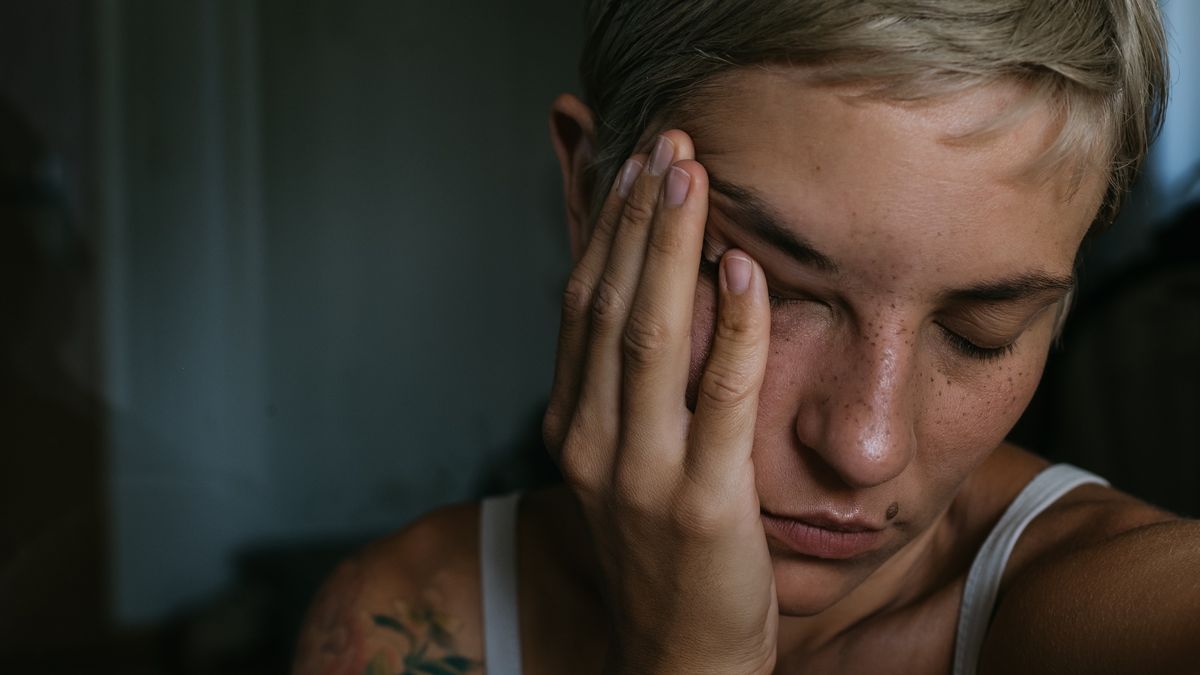 A dramatic dark closeup portrait of a young woman
A horizontal closeup portrait of a young woman in natural lighting on a dark background holding hand to face with short dyed blond hair with closed eyes and skin texture and freckles makeup with a birthmark on face and flower tattoos looking tired or having a headache
Kateryna Zasukhina