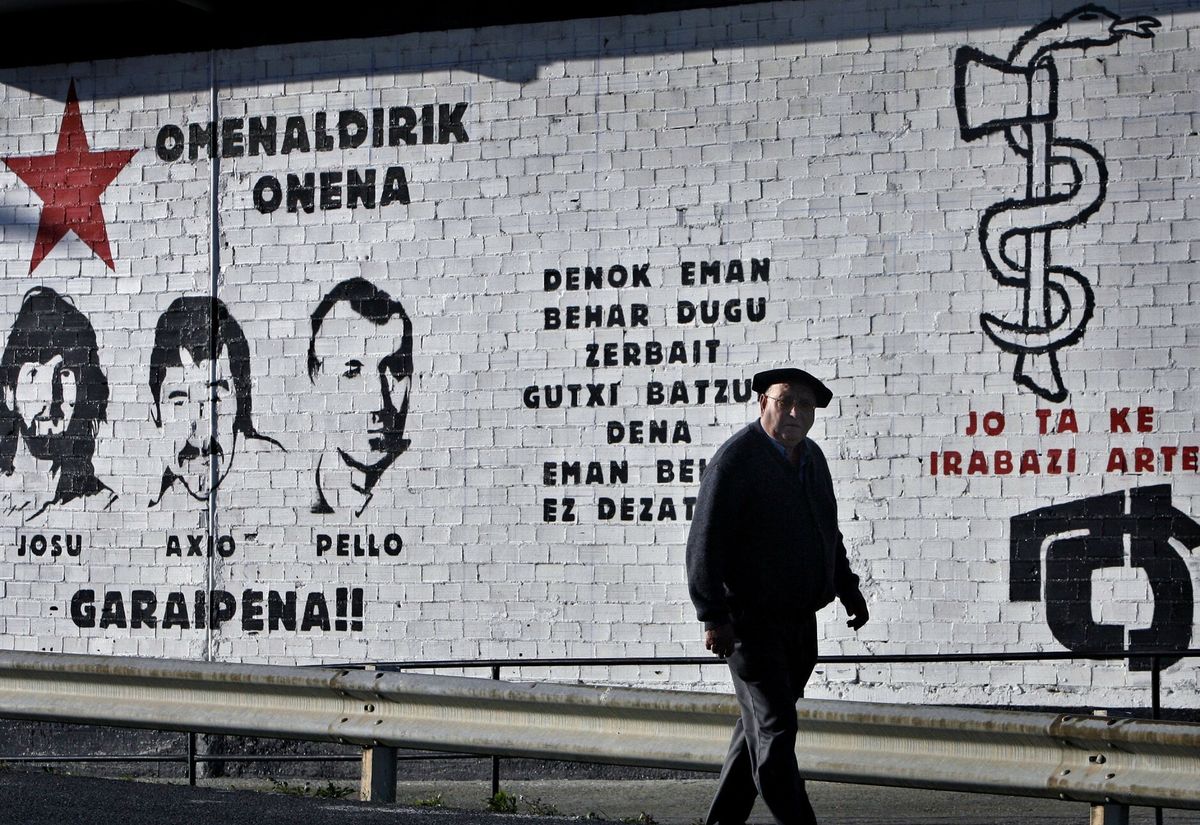 Mężczyzna idzie przed malowidłem ściennym z twarzami i nazwiskami trzech zmarłych  członków zbrojnej grupy baskijskich separatystów ETA