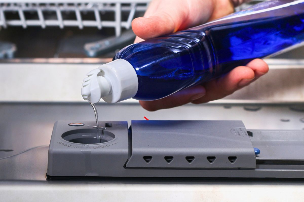 The man is applying detergent to the dishwasher.