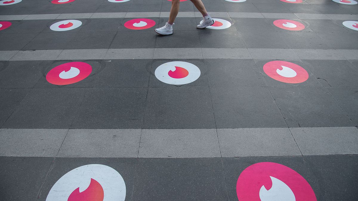 BANGKOK, THAILAND - 2022/02/13: A woman seen walking past social distancing tinder logo markers at the Trimurti Shrine in Bangkok.
 The "Pray and swipe right" event organized by online dating app Tinder, with Social distancing Tinder logo markers on the praying ground, a photo booth where people can take profile pictures for their new accounts, and free offering sets, at the Trimuriti shrine on Valentine's day in Bangkok, Thailand. The Trimuriti one of the Hindu gods is known to be the god of love. People come to worship at the Trimurti shrine with offerings of red roses in the hope that they will meet their soulmate. (Photo by Peerapon Boonyakiat/SOPA Images/LightRocket via Getty Images)