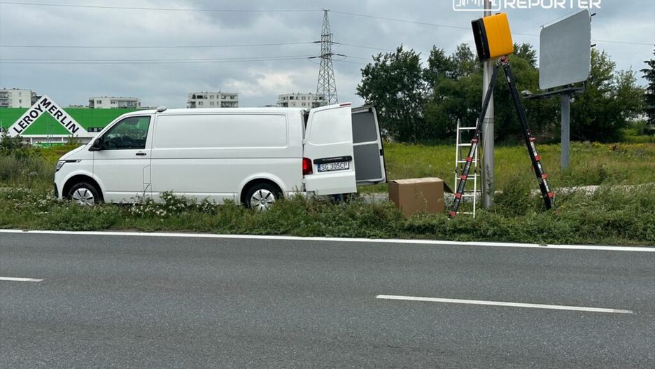 Biały van zaparkowany przy drodze, obok drabina i karton, w tle widoczny znak reklamowy Leroy Merlin.