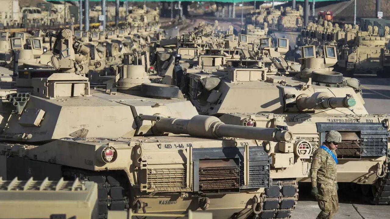 A soldier walking past a row of M1 Abrams tanks