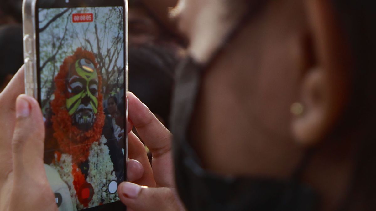 A woman takes a photo of a Koragajja Theyyam performer on her mobile phone as he participates in the 42nd Cochin Carnival in Fort Kochi, India, on January 1, 2026. The Carnival is held annually to welcome the start of the New Year. (Photo by Sivaram Venkitasubramanian/NurPhoto via Getty Images)