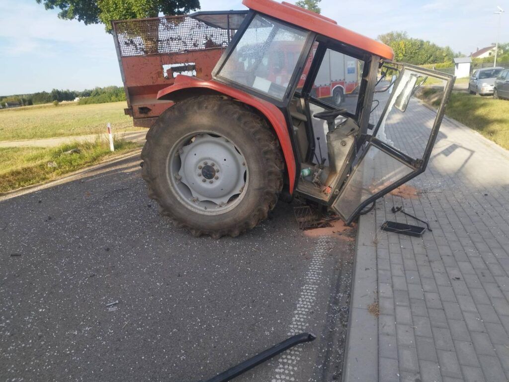 Traktor z otwartymi drzwiami stoi na poboczu drogi, obok leżą fragmenty szkła i odłamki.